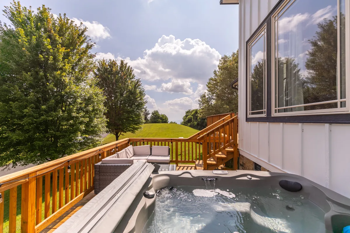 A peaceful view of the outdoor hot tub nestled on the deck, surrounded by ample seating and overlooking a picturesque landscape. The lighting hints at both sunrise and sunset moments, inviting relaxation and spa-like indulgence.