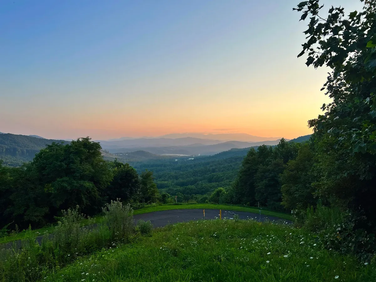 A breathtaking wide-angle view of rolling hills, distant mountains, and a sunset sky with a meandering road. The image conveys tranquility and the immense natural beauty of the region—perfect for hiking, photography, and nature appreciation.