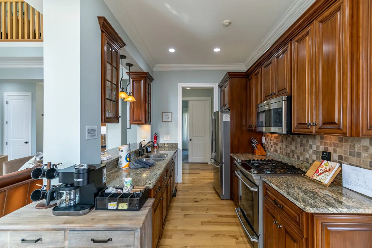 This image showcases a chef’s kitchen featuring granite countertops, stainless steel appliances, a central kitchen island, and warm wood cabinetry. The space is well-lit and designed for both cooking and gathering, with plenty of room for group meal preparation or casual conversation while cooking.