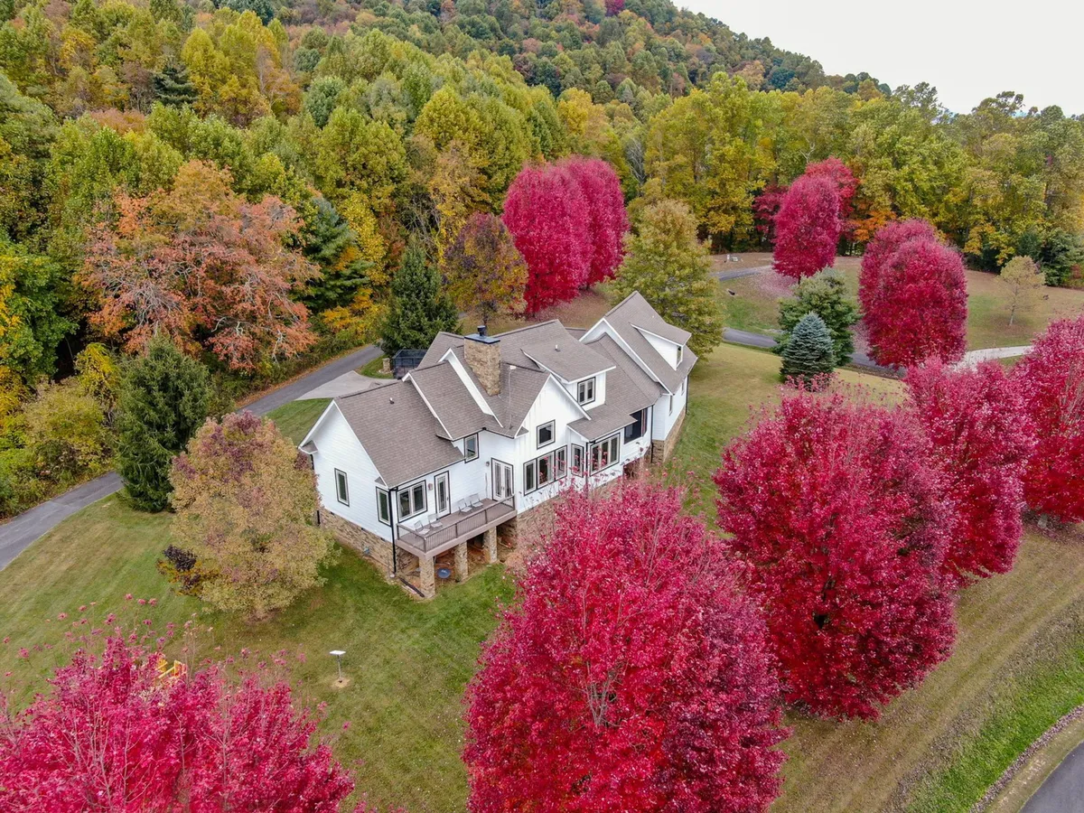 This image showcases the house nestled among vibrant red trees and surrounded by lush nature, exemplifying the striking autumn foliage and the property's dramatic setting. The porch and yard offer inviting spaces for outdoor gatherings and appreciating the change of seasons.