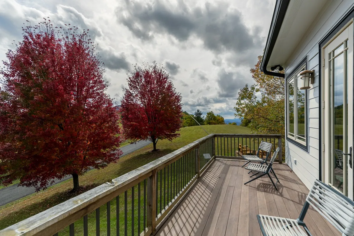 This exterior scene presents a tranquil deck lined with red trees, comfortable deck chairs, and a sweeping landscape view. The mood is peaceful, perfect for relaxation, sunset watching, or morning coffee surrounded by nature.