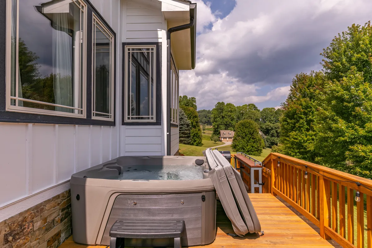 A tranquil outdoor deck featuring a bubbling hot tub with views of the surrounding natural landscape. The setting is peaceful, with wooden decking and lush greenery, suggesting relaxation and indulgence after a day of exploration.