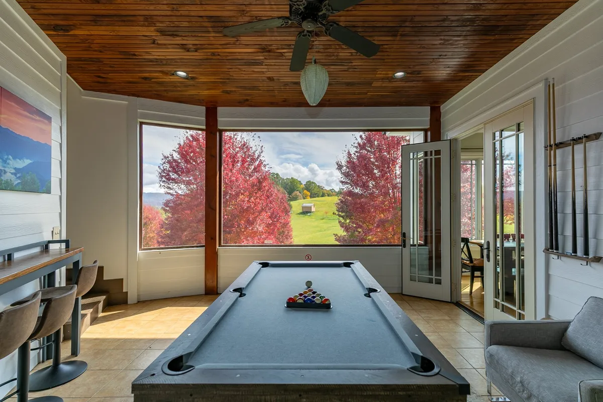 This cheerful interior shot captures a pool table set beside large windows that reveal brilliant autumn trees outside. The bar seating and spacious setup make this room ideal for socializing, playing games, and enjoying the sunset views. The overall mood is bright and welcoming, emphasizing the room’s function as a hub for activity and camaraderie.