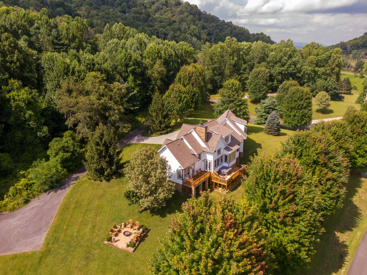 This image captures the exterior of the house featuring the deck and fire pit area, framed by surrounding trees. The scene is set around dusk, giving a serene atmosphere, with hints of outdoor gathering spaces ideal for family barbecues or evenings by the fire pit.