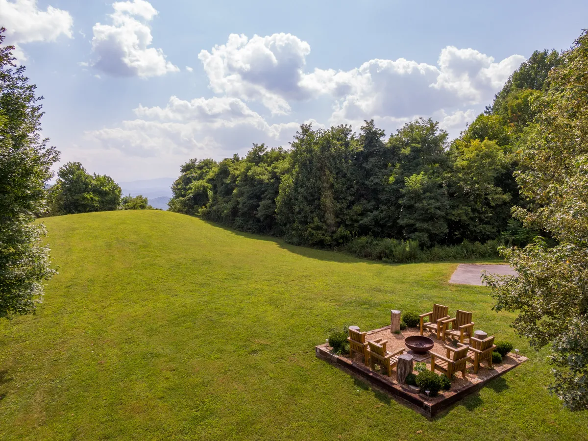 A cozy fire pit area surrounded by greenery and distant hills, providing a perfect outdoor gathering spot. The setting evokes a peaceful, campfire atmosphere, ideal for evenings of relaxation under the stars.